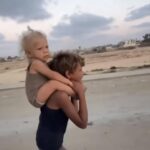 طفل فلسطيني يحمل شقيقته رمز المعاناة الإنسانية في غزة